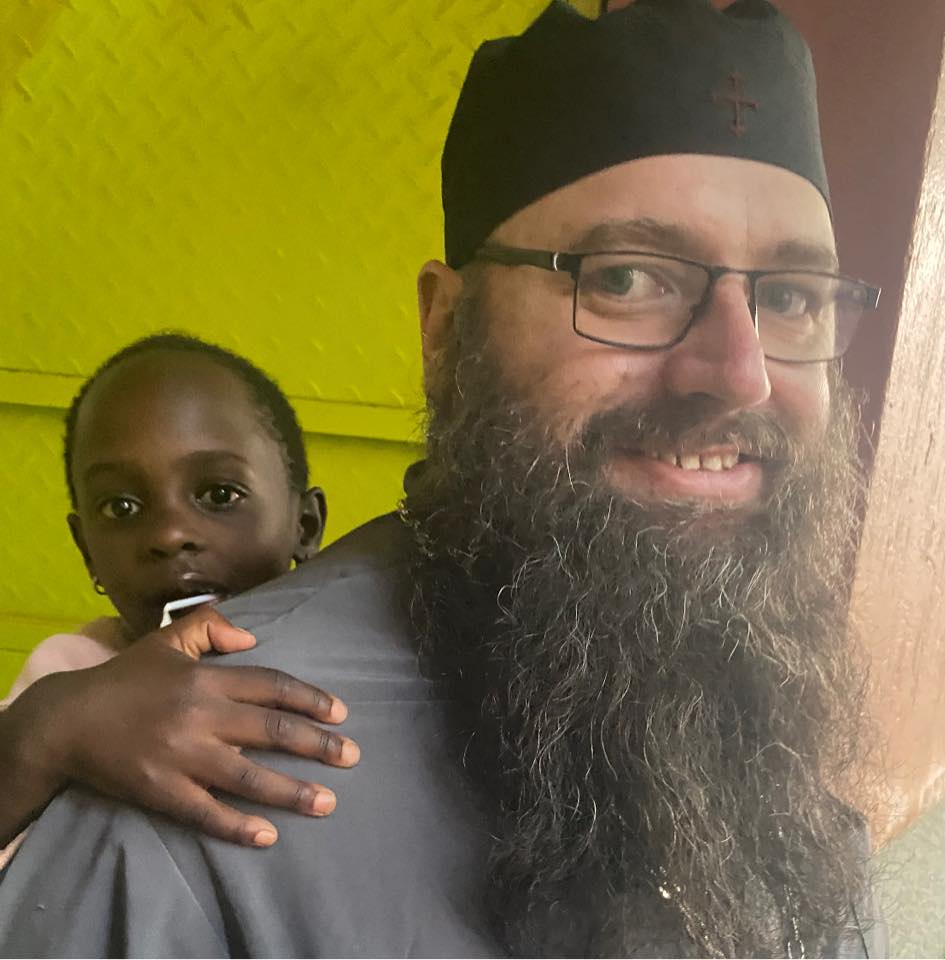 Fr. Silouan Brown serving the Lord in Uganda, carrying a child on his back.